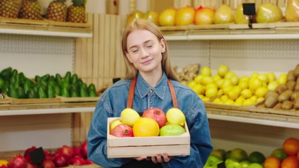 Улыбающаяся большая леди с сундуком, полным органических фруктов позирует перед камерой в магазине органических овощей — стоковое видео