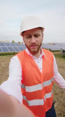 Yenilenebilir enerji ve ekolojik yenilik kavramı güneş enerjisi santralinde. Bir ekoloji çalışanı selfie videosu çekiyor. Güvenlik kaskı taktığı güneş panellerinden bahsediyor.