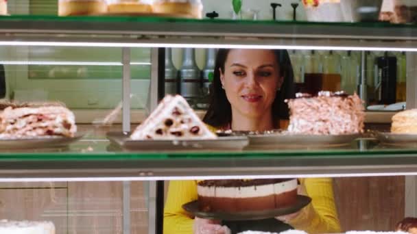 In the coffee shop the saleswoman take some cakes and arrange them in the showcase fridge capturing some tasty sweet dessert — Vídeo de Stock