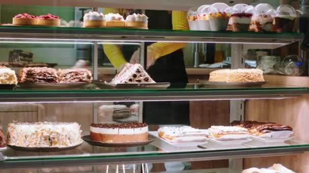 Im Café arrangiert Verkäuferin mit Schutzmaske die Desserts aus dem Vitrinen-Kühlschrank sehr sorgfältig — Stockvideo