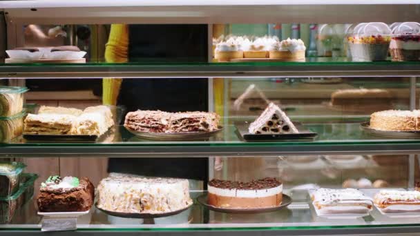 Leuke bakkerij cafe in de voorkant van de camera verkoopster met een beschermend masker neem wat taart uit de vitrine koelkast te verkopen voor de klant — Stockvideo