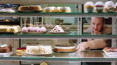 Girişimci ve küçük işletme yemekleri ve restoran yemekleri kavramı. Genç satıcı, vitrin dolabını açar ve vitrine taze çöl koyar.