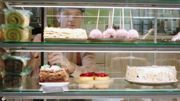 In de pandemie van coronavirus verkoper met beschermend masker verbluffend in bakkerij cafe opent hij de vitrine koelkast en neemt een aantal woestijnen om te verkopen — Stockvideo