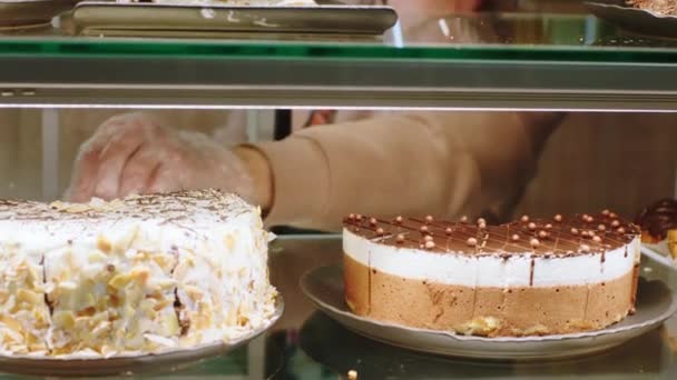 Taking details in the bakery cafe salesman arrange the deserts from the showcase fridge very carefully — Stock Video