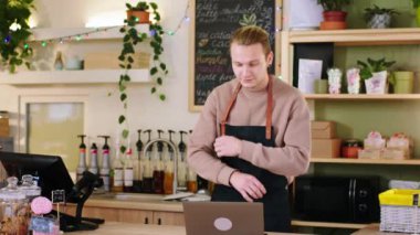 Kahve dükkanında yakışıklı bir genç adam bilgisayarına bir şey yazıyor sonra kameraya bakıyor ve büyük bir gülümseme sergiliyor.