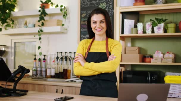 Concept de petite entreprise belle femme mature barista posant devant la caméra dans le café, elle croise les mains et regarde directement à la caméra — Video