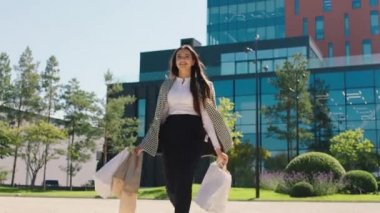 Ekolojik alışveriş torbalarıyla gezen iş kadını kameranın önünde gülümsüyor ve güneşli günün tadını çıkarıyor.