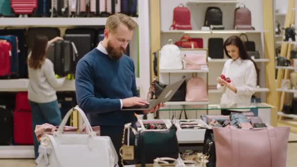 Dans un grand magasin d'accessoires superviseur homme utilisant un ordinateur portable pour vérifier les choses des magasins tandis que d'autres travailleurs sont organiser les choses sur le fond — Video
