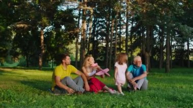 Karizmatik genç ebeveynler, iki çocukları ve büyükbabalarıyla birlikte parkın ortasında büyük uçaklarla oynarken eğleniyorlar.
