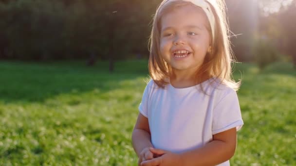 一个漂亮可爱的小女孩看着公园中央的相机，微笑着站在相机旁边，非常迷人 — 图库视频影像