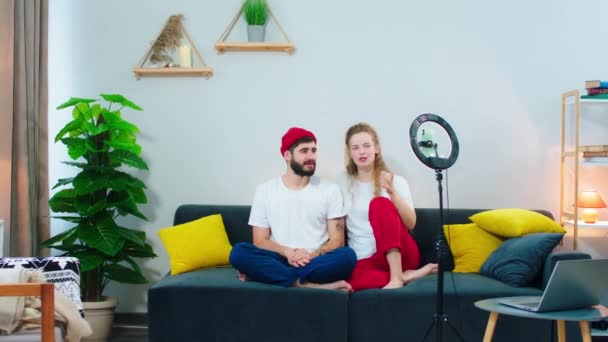 Attractive young couple at home in living room make a live stream they talking about something for the social media account using a light ring for the stream — 图库视频影像