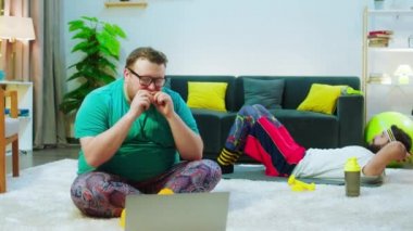Aç obez adam evde hamburger yiyor ve arka planda arkadaşları altılı bira almak için mekik çekerken dizüstü bilgisayardan bir şeyler izliyor. ARRI Alexa 'da çekim