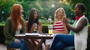 In the middle of the park at the cafe group of amazing looking ladies multiracial have a chill time together cheers with lemonade and feeling happy