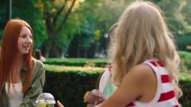 Great looking group of young women enjoy the moment together at the cafe in the middle of the park they taking some lemonade and discussing all together