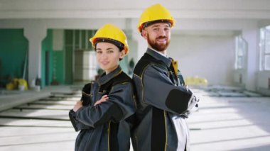 Posing in front of the camera good looking man engineer and beautiful woman architect they standing in the middle of construction site