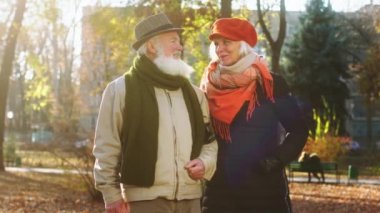 Happy and romantic old couple posing in front of the camera in the middle of the park in a cold autumn day