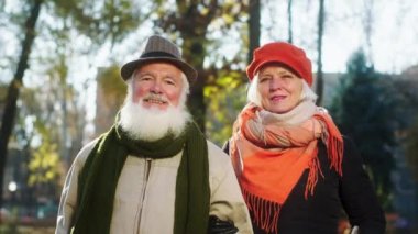In a perfect sunny day in the autumn attractive old couple posing in front of the camera in the middle of the park they are very cute and beautiful