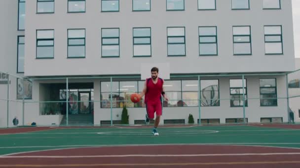 Attractive man in a red sport suit playing basketball in a large stadium he running concentrated after the ball — Vídeo de Stock