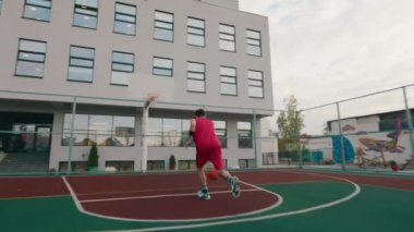 Basketbol oynayan kırmızı takım elbiseli genç adam topu büyük, modern bir stadyumda sepete attı.