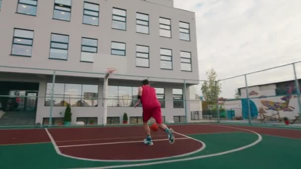 Grając w koszykówkę młody człowiek w czerwonym stroju sportowym rzuca piłkę do kosza na dużym nowoczesnym stadionie — Wideo stockowe