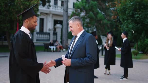 In the college garden happy black student in his graduation day take his diploma from the college professor then they posing in front of the camera very excited multiethnic concept — Video Stock