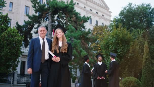 In the college garden beautiful lady student graduate posing excited with her diploma with the college professor in front of the camera — Wideo stockowe