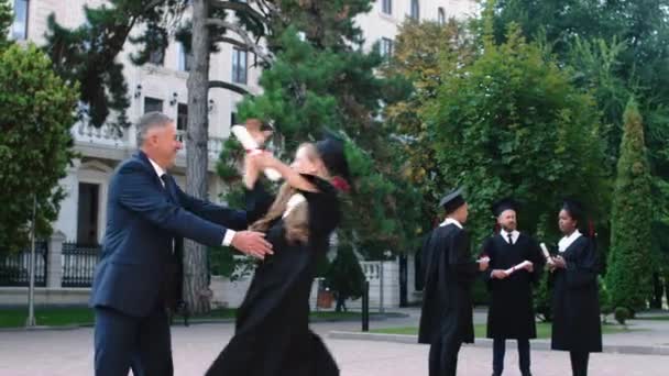 Beautiful lady after she was graduate running to his dad very excited hugging him and start to telling something she holding her diploma — Vídeos de Stock