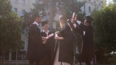 Excited and happy students graduates after they take their diplomas dancing and jumping in the college garden wearing graduation suits and caps
