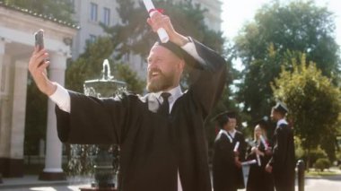 Great looking man student after he was graduate called someone on the smartphone turn on the camera show the diploma he was feeling excited and happy