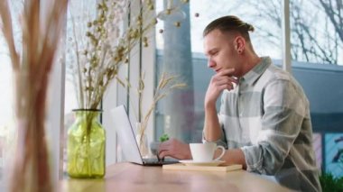 Good looking man at coffee shop using his laptop to studying online he make a thinking face while drinking his coffee. 4k