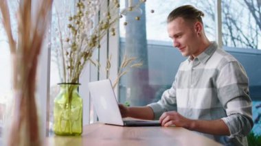 Good looking happy guy closeup his laptop after he end his online courses while sitting at the coffee shop beside the big panoramic window. Shot on ARRI Alexa Mini