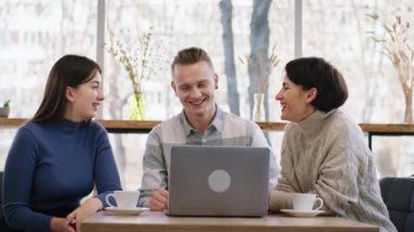 In the cozy coffee shop group of students multiracial using the laptop to make a project together they discussing smiling large and drinks some coffee
