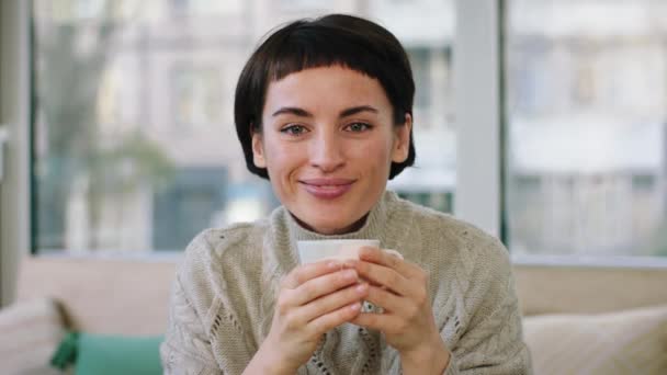 Mujer de aspecto perfecto con una bonita sonrisa posando delante de la cámara de cerca sonriendo a lo grande y sosteniendo una taza de café — Vídeo de stock