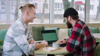 At the coffee shop two charismatic and attractive men discussing about some project while using the laptop they smiling large and feeling excited. Shot on ARRI Alexa Mini
