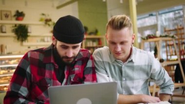 Happy two charismatic guys watching some show on the laptop and excited hugging each other while drinking some coffee in the cafe