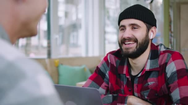 Good looking guy at the coffee shop have a conversation with his friend smiling large and have a funny discussion together — Stock video