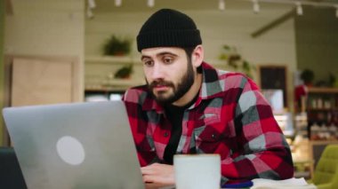 In front of the camera excited and happy guy watching something on the laptop and get very excited after his find something at the coffee shop