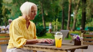 Old business woman working on the laptop in the middle of the park at the cafe she using the laptop to write something