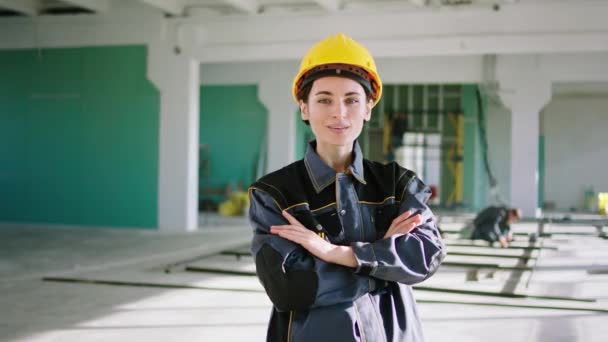 Kameranın önünde güzel bir gülümseme ile güzel bir kadın mühendis pozu vererek inşaat binasının ortasında büyük baharatla duruyor ve güvenlik kaskı ve üniforması giyiyor. 4k — Stok video