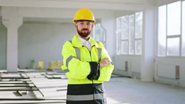 Beautiful young engineer man posing to the camera at construction site he crossing hands and wearing uniform and safety helmet
