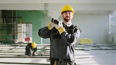 In front of the camera good looking man construction worker working hard at construction site he carrying the building materials and wearing protective helmet and special uniform