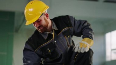 In the modern construction building working closeup to the camera construction worker man he painting a building material with a small brush and wearing safety helmet and equipment