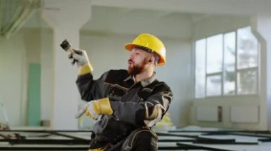 In front of the camera charismatic dancing constructor worker man with safety helmet and uniform while working at construction site dancing while listening music from the wireless earphones