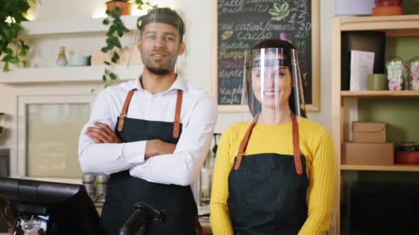 Beau Afro-Américain homme barista et sa collègue dame barista multiracial posant devant la caméra dans le café ils portent un masque de protection — Video