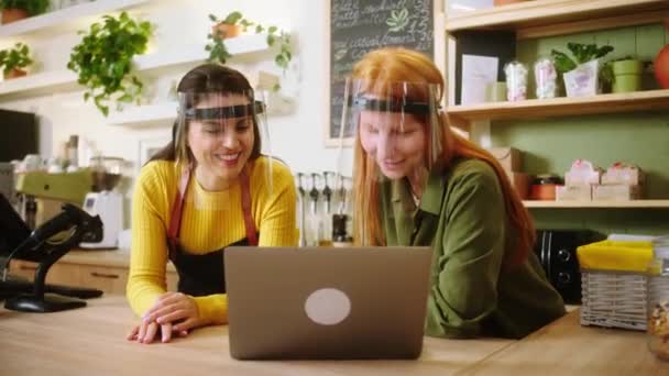 Matka a dcera pracují společně ve své kavárně pomocí notebooku na hledání něčeho, co mají na sobě ochranné masky v pandemii koronaviru — Stock video