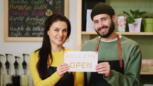 Jóképű barista férfi és a kávézó tulajdonosa nő előtt a kamera pózol egy nyitott táblák és mosolygós nagy koncepció a kisvállalkozás és a vállalkozó — Stock videók
