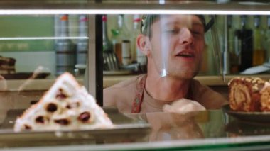 Lezzetli fırın kafesinde kamera satıcısına çok yakın çekim yaparken çok karizmatik bir şekilde vitrin dolabına taze çöl ekleyin. Koronavirüs salgınında koruyucu maske takıyor. - Evet. Atış açık.