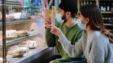 Kahve dükkanında iki karizmatik genç bayan ve koruyucu maskeli adam marketteki buzdolabına bakıyor ve tatlı seçiyorlar.