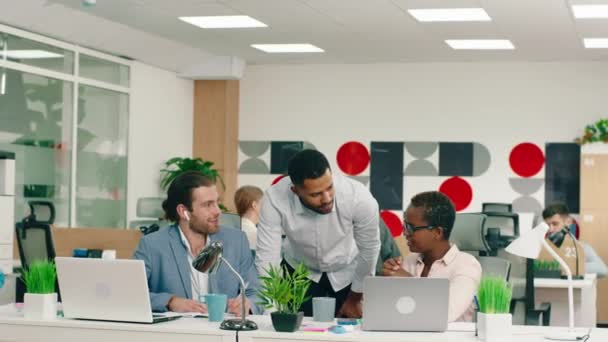 Δύο Αφρικανοί συνάδελφοι συζητούν για δουλειά ο ένας στον άλλο σε ένα μεγάλο μοντέρνο γραφείο, ενώ ένας όμορφος άντρας δίπλα τους κάνει τη δουλειά του. — Αρχείο Βίντεο