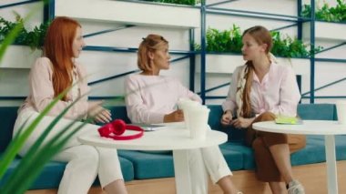 Üç güzel sarışın kadın kahve masasında oturmuş sohbet ediyorlar.